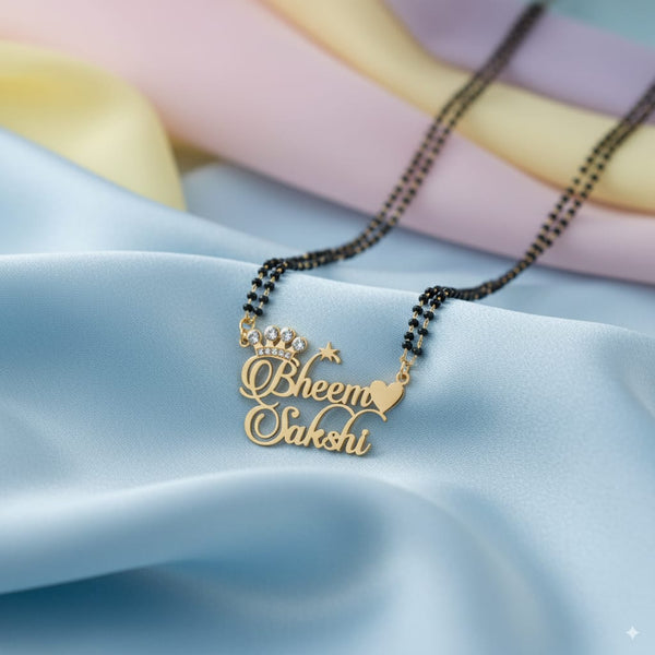 Personalized couple name mangalsutra with gold-plated pendant featuring heart and crown design, engraved with names Sonu and Sheetal, placed on royal blue fabric background.
